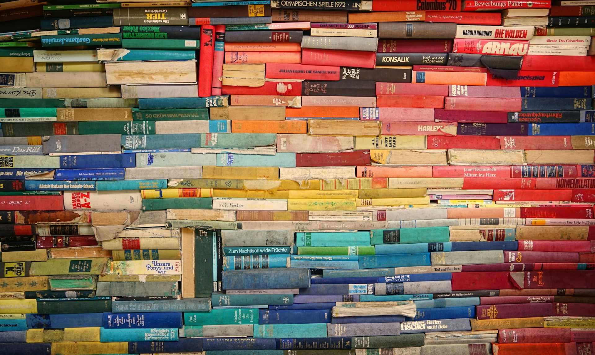 A pile of books stacked spine-first in a rainbow of colours.